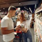 A young couple looking at canned goods in a supermarket aisle, shopping together.